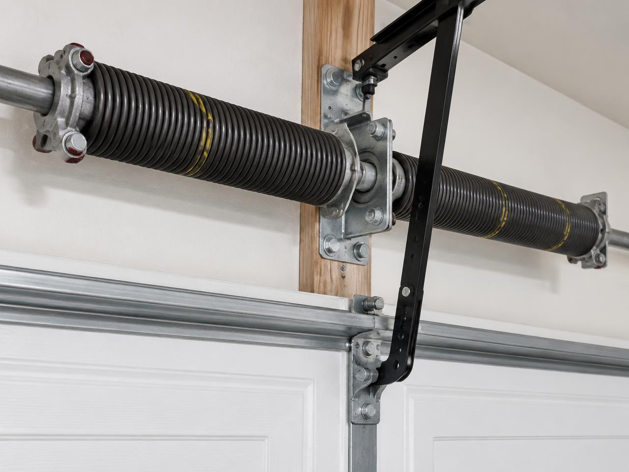 Technician inspecting a garage door torsion spring and shaft above a residential garage door